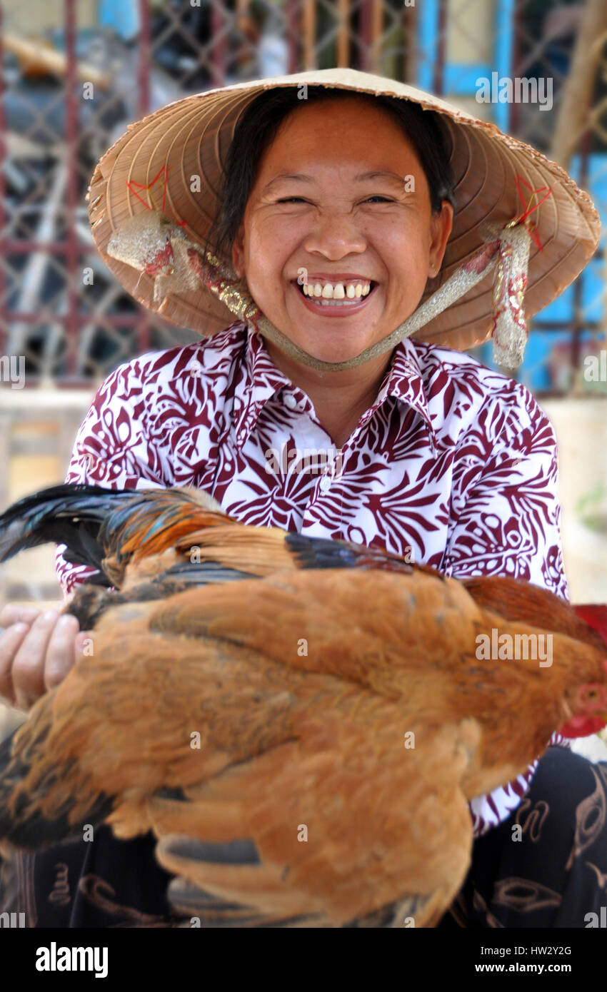 Un felice fornitore offre un pollo vivo per la vendita in mercati di Hoi An nel Vietnam centrale. Foto Stock