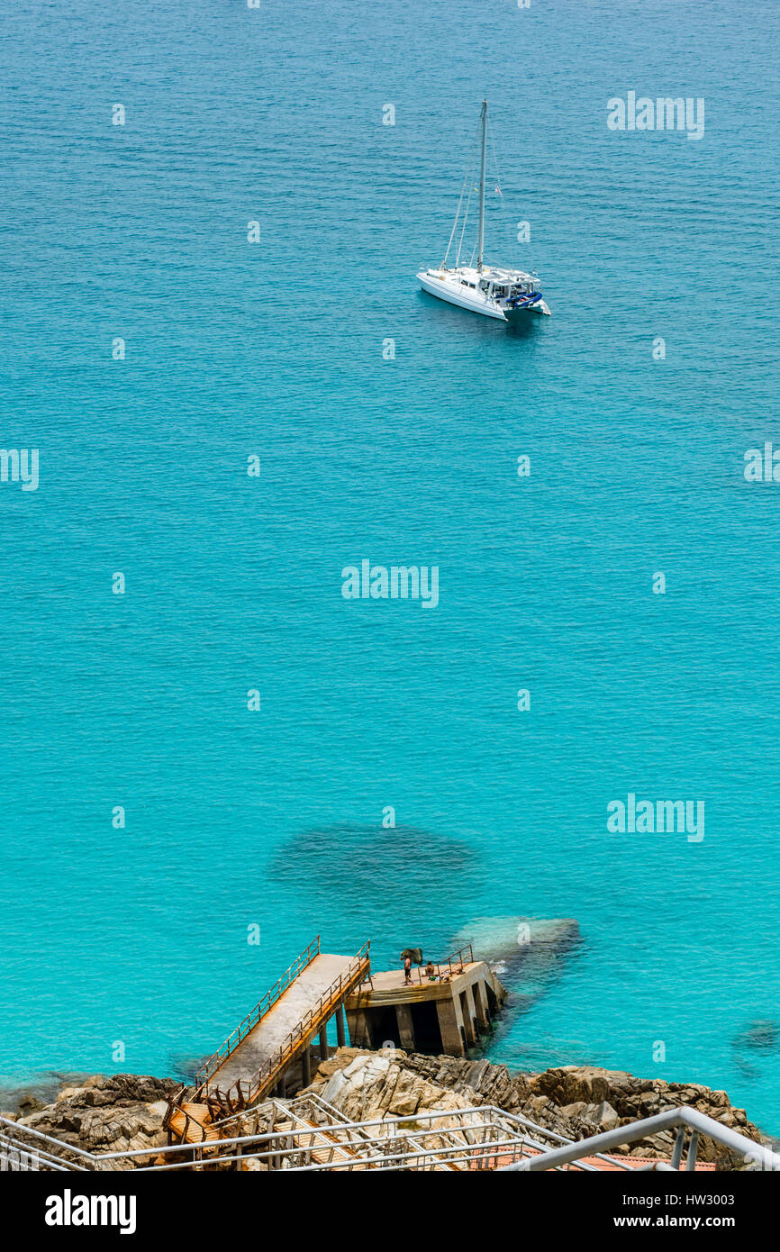 Un gruppo di persone di crogiolarvi al sole su un molo rotto con yacht in mare, Pulau Perhentian Kecil, Malaysia. Foto Stock