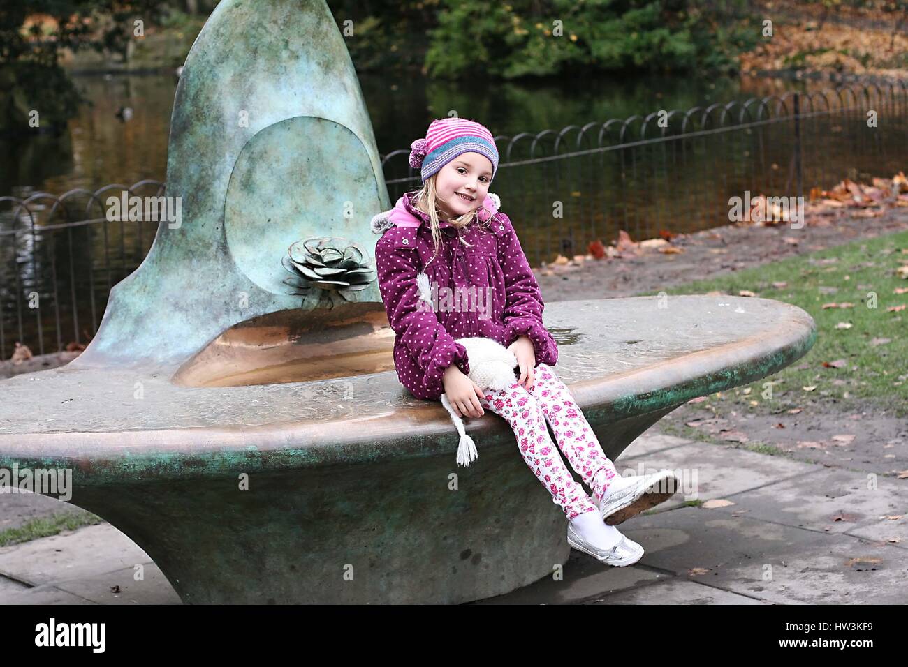 Bambina, bambino, kid divertirsi seduti fontana a giocare tra le foglie di autunno nel parco di St. Stephen's Green, Dublino Irlanda concetto di infanzia Foto Stock