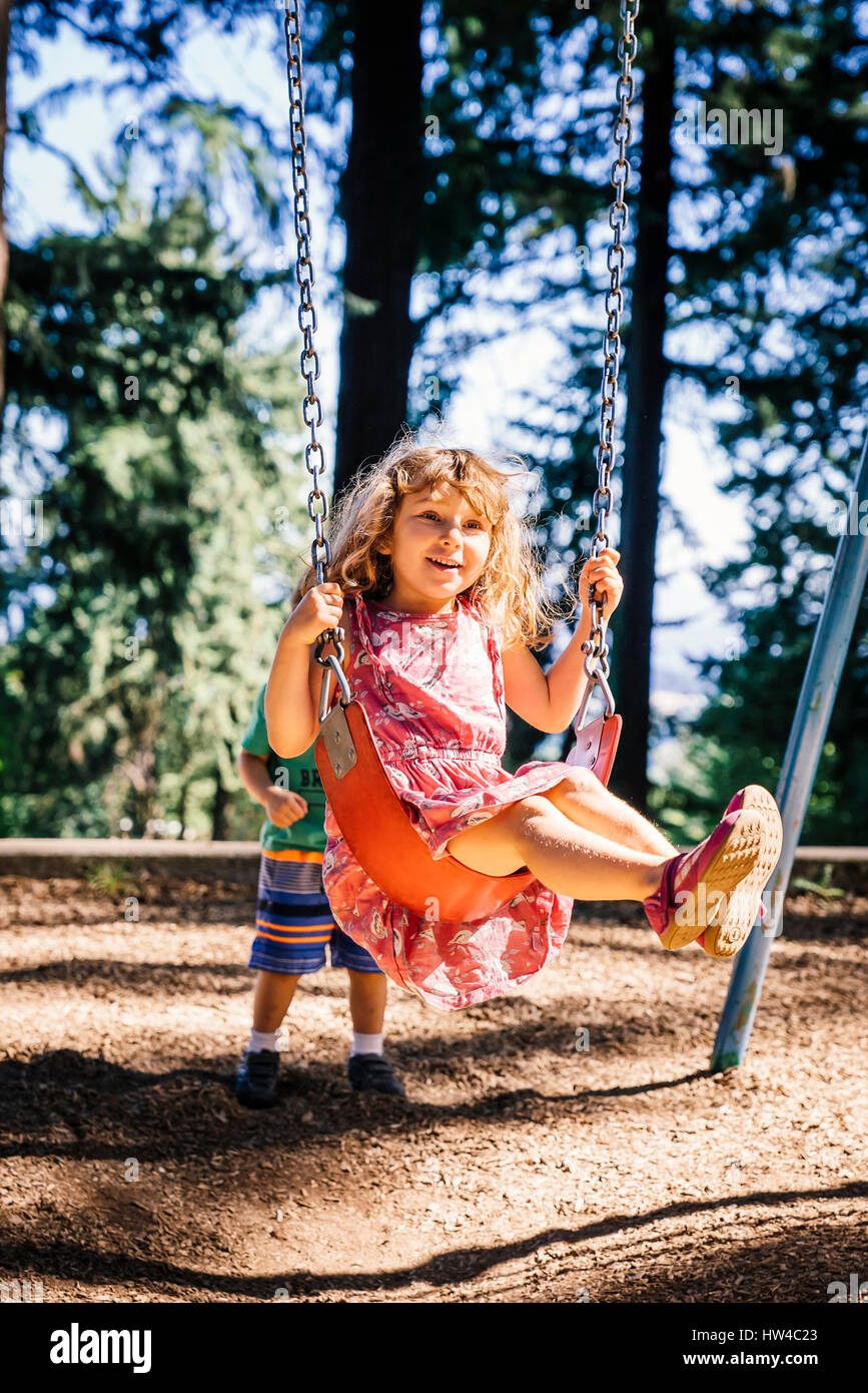 Ragazzo caucasico spingendo sorella sul parco giochi swing Foto Stock