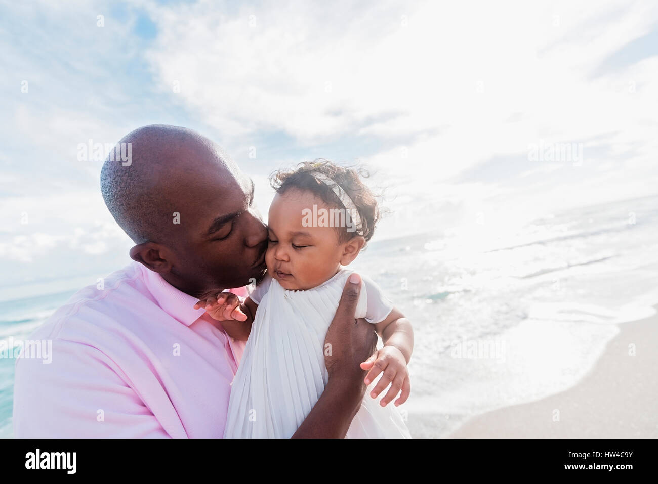 Padre baciare guance della bambina sulla spiaggia Foto Stock