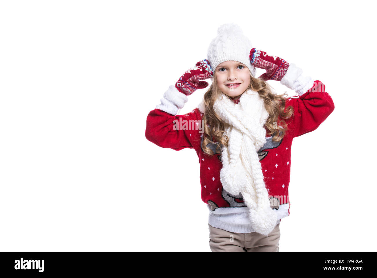 Carino sorridente bambina con capelli ricci indossare pullover a maglia, sciarpa e cappello e guanti isolati su sfondo bianco. Abbigliamento invernale Foto Stock