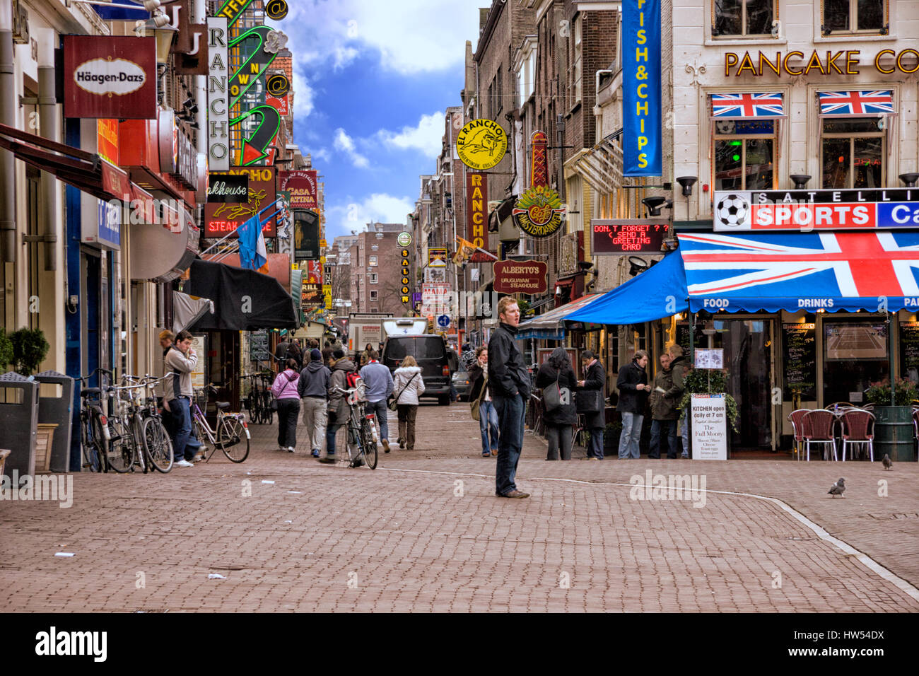 Persone in piedi e a camminare in una strada acciottolata a Amsterdam, Paesi Bassi Foto Stock