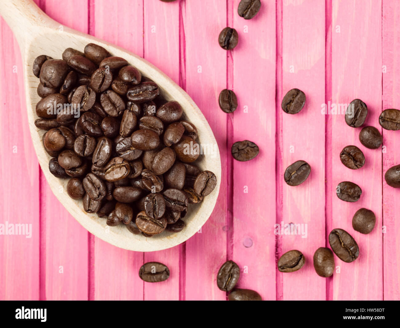 1 cucchiaio di estratto secco di chicchi di caffè tostati contro un sfondo rosa Foto Stock