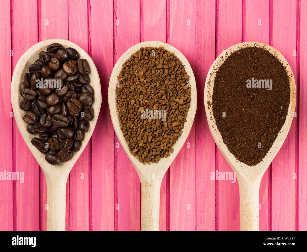 Cucchiai di instant granulate e arrostire i chicchi di caffè contro un sfondo rosa Foto Stock