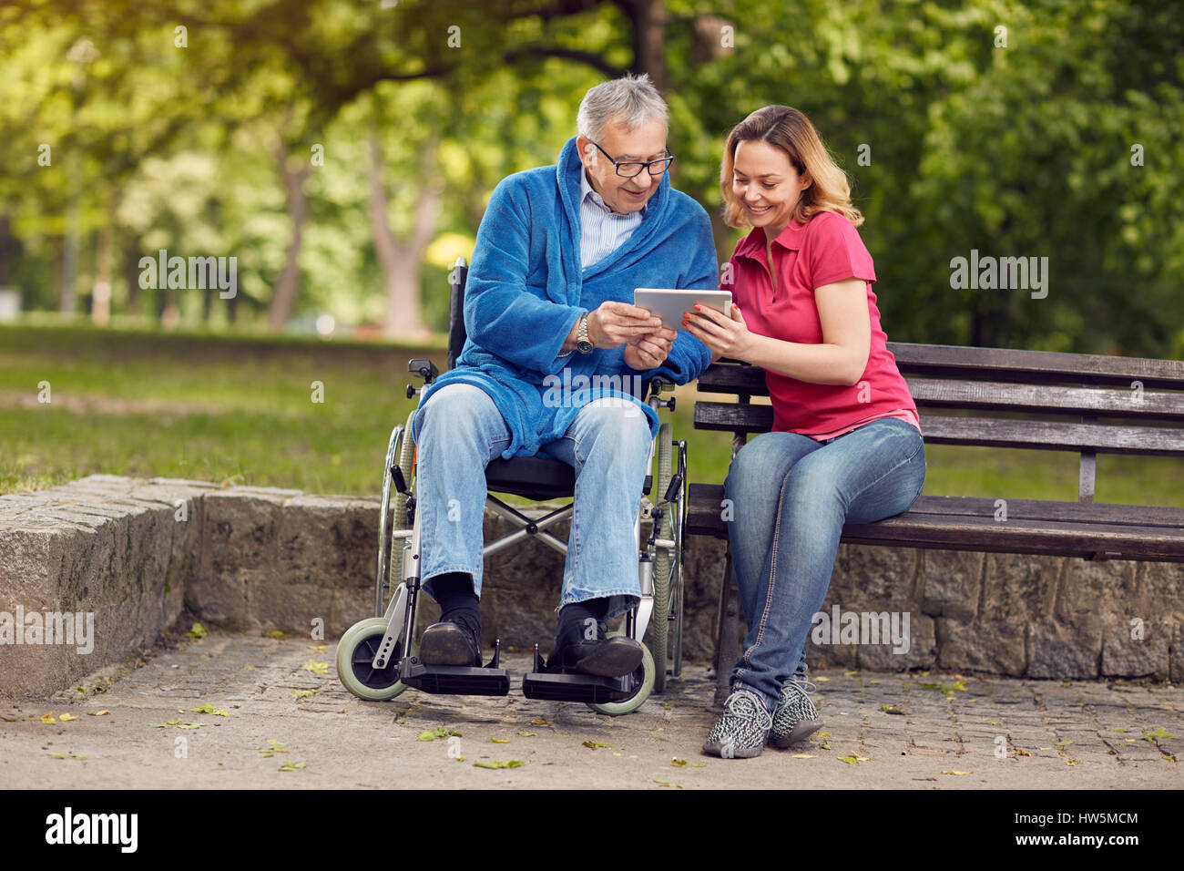 Felice l'uomo in sedia a rotelle con la figlia utilizzando tablet nel parco Foto Stock