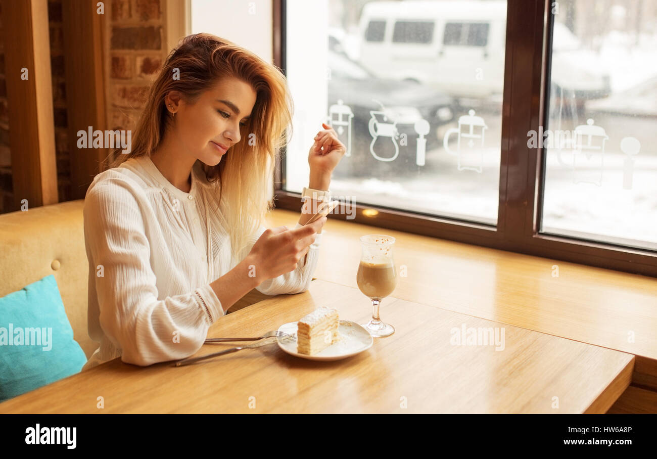 Una ragazza è seduto in un bar e utilizzando uno smartphone, la digitazione sul telefono Foto Stock