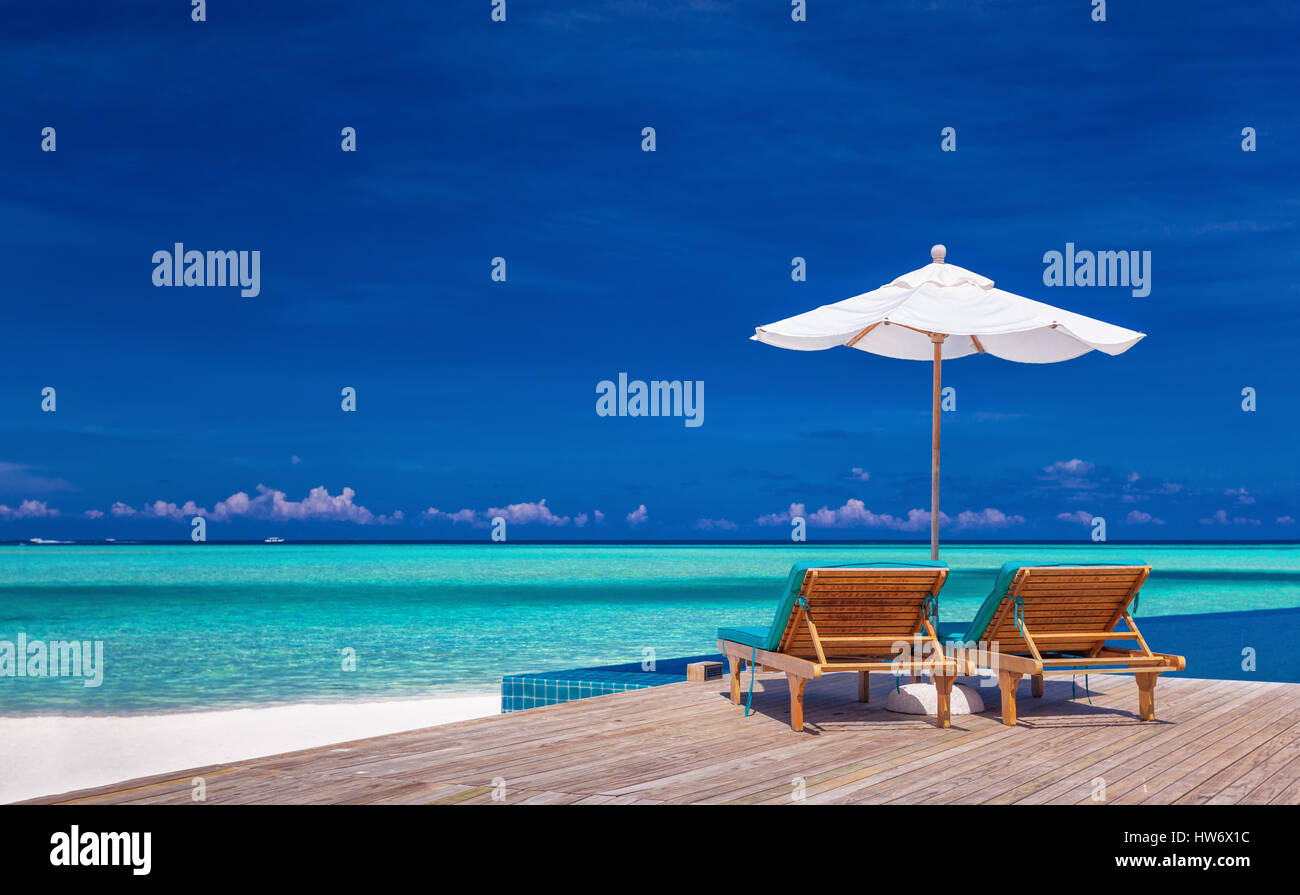 Sedie a sdraio con ombrellone affacciato sulla piscina infinity e laguna tropicale Foto Stock