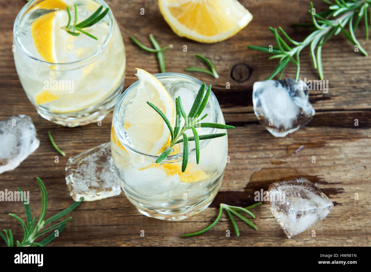 La bevanda alcolica (gin tonic cocktail) con limone e rosmarino e ghiaccio su tavola in legno rustico, spazio di copia Foto Stock