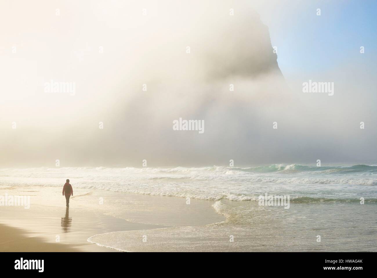 Norvegia, Nordland, isole Lofoten, isola Moskenesoy, donna camminando lungo la spiaggia isolata di Kvalvika, rottura sole attraverso la nebbia Foto Stock