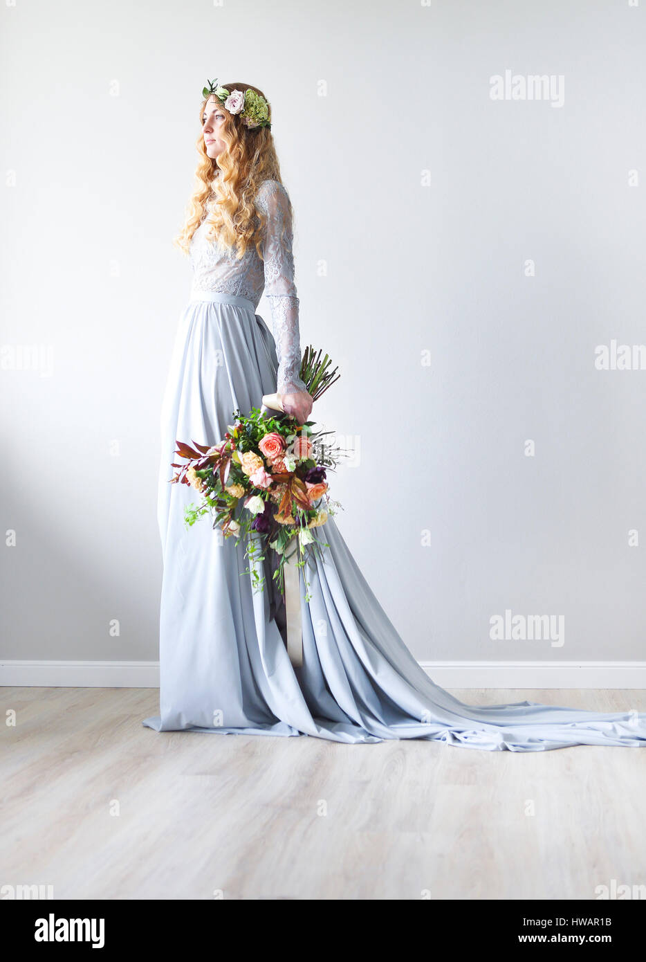 Primavera di bellezza ritratto di una sposa con una ghirlanda e un mazzo di fiori in mano con il muro grigio Foto Stock