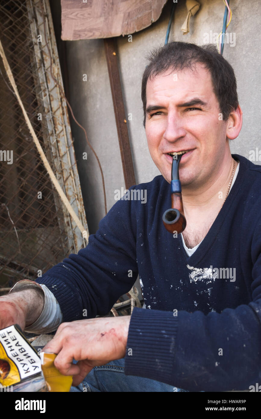 Krasnodar, Russia - 4 Marzo 2017: giovani adulti sorridente russo fumi di macellaio tubo dopo un abbattimento di un toro, testo russo sul tabacco casella significa Smok Foto Stock