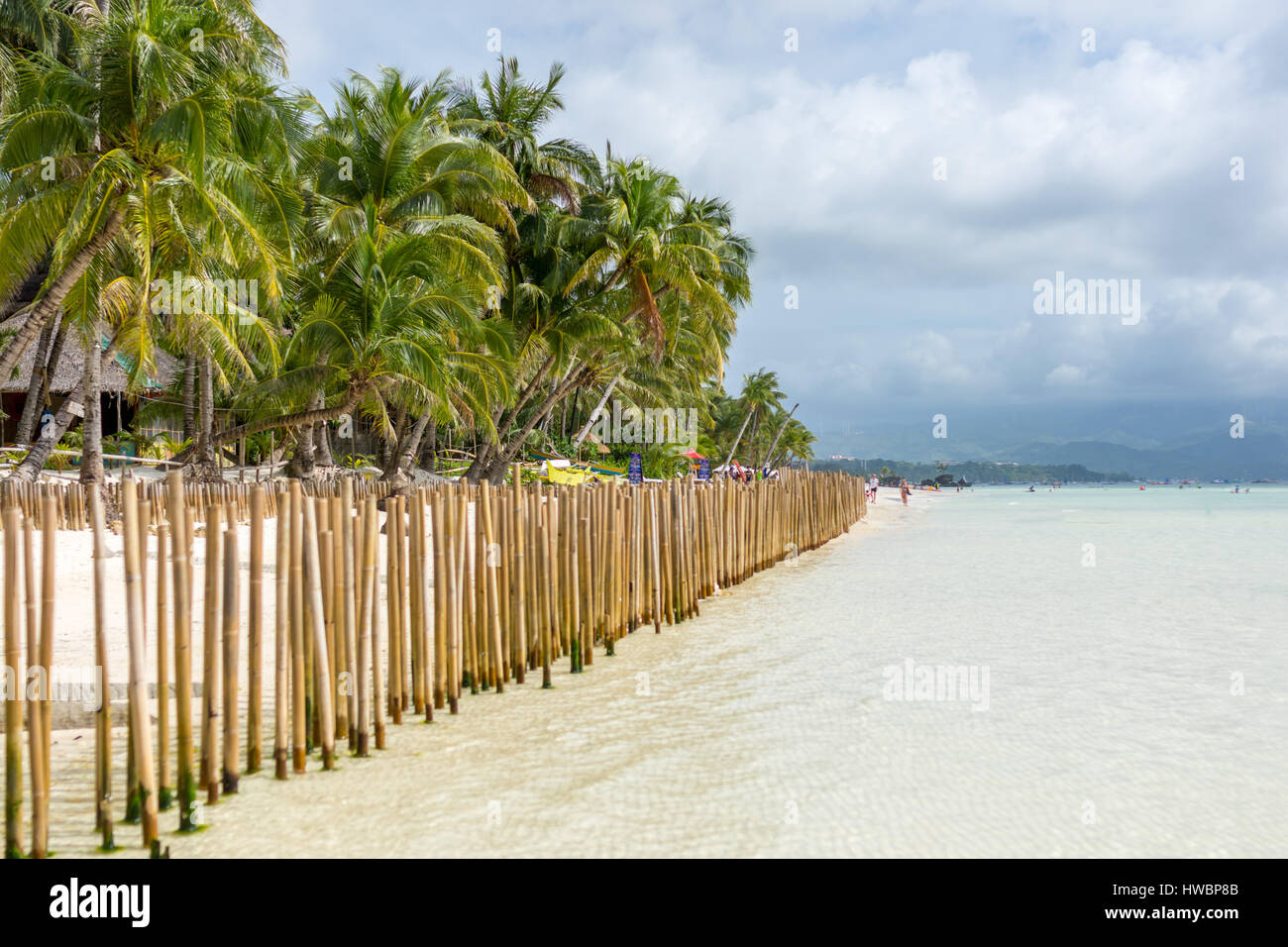 Guardando verso il basso una barriera di recinzione fatta di poli di bambù in un'isola tropicale di spiaggia di sabbia bianca con un palm alberata a riva e il promontorio collinare in distanc Foto Stock
