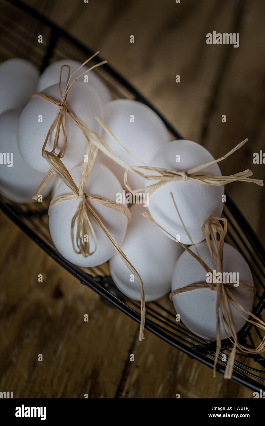 Bianco fresco Uova legata con una stringa in un cesto su uno sfondo di legno, fuoco selettivo immagine, concetto di pasqua Foto Stock