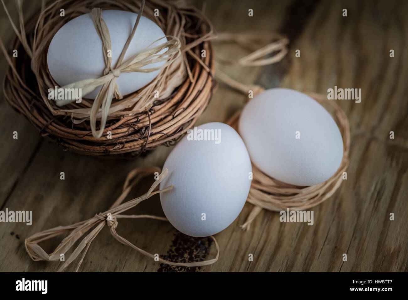 Tre le uova bianche uno nel nido su sfondo di legno, fuoco selettivo immagine concetto di pasqua Foto Stock