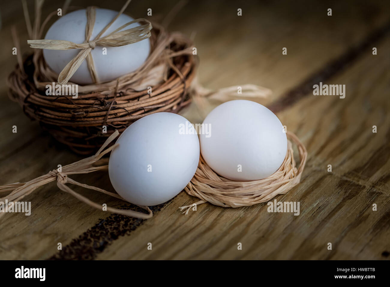 Tre le uova bianche uno nel nido su sfondo di legno, fuoco selettivo immagine concetto di pasqua Foto Stock