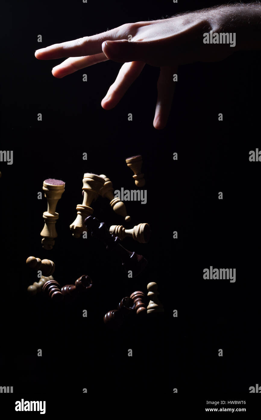Una mano lasciandosi a scacchi pezzi cadono al suolo, isolato di fronte a uno sfondo nero Foto Stock
