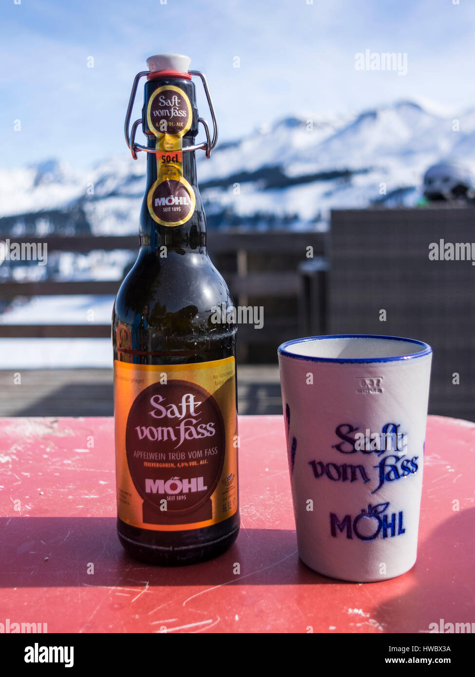 Bottiglia di Möhl Apfelwein 'Saft vom Fass', un tradizionale svizzero di sidro, con un bicchiere di ceramica. Sfondo alpino. Foto Stock