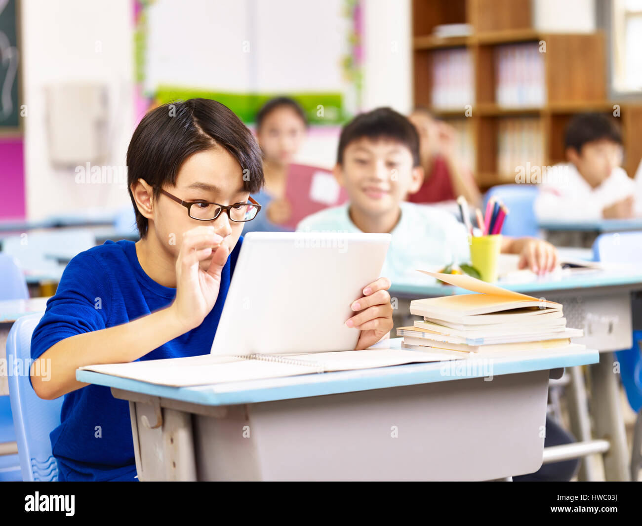 Elementare asiatici schoolboy guardando con curiosità a un computer tablet detenute dal suo compagno, focus sul ragazzo in primo piano. Foto Stock
