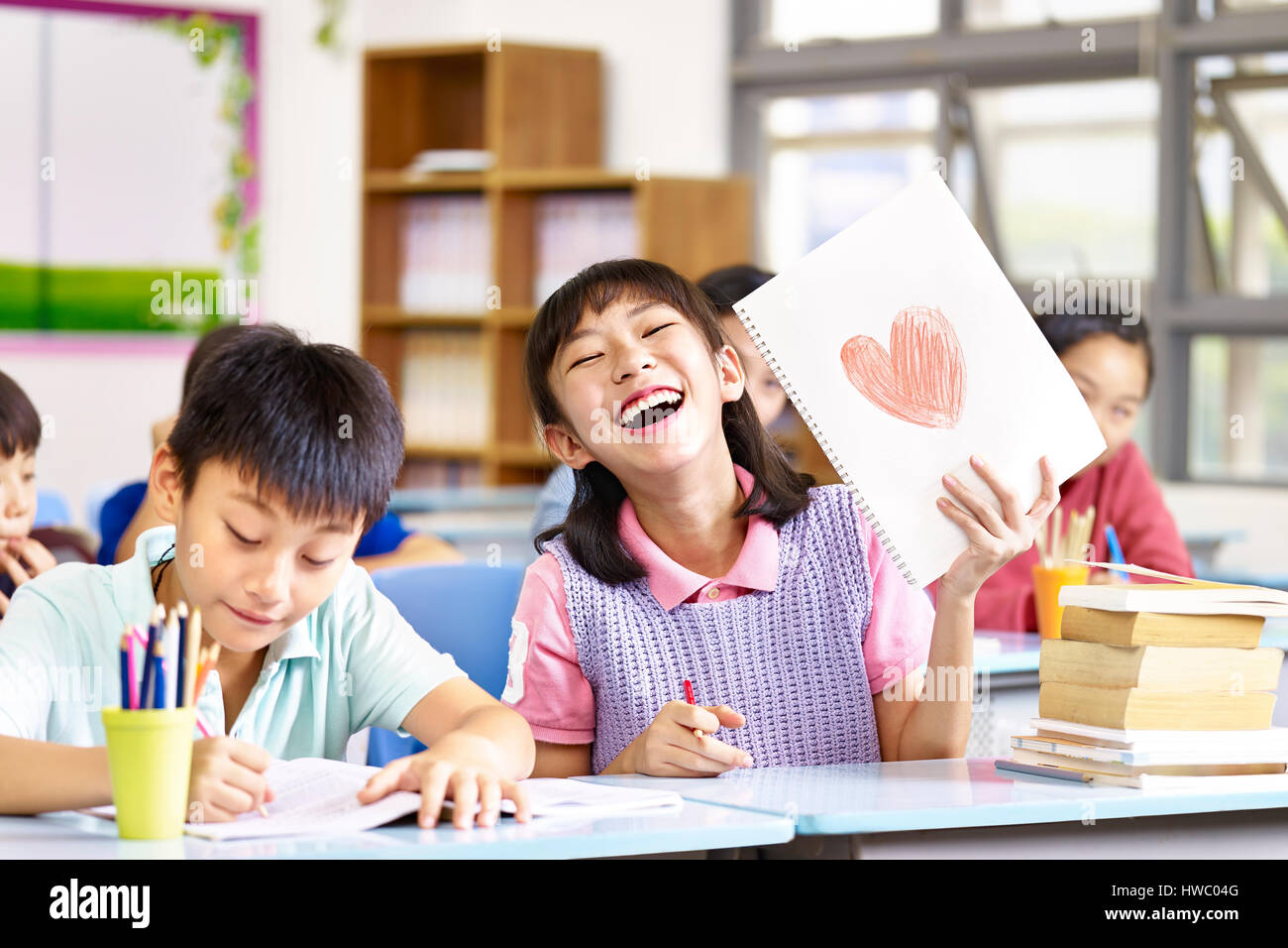 Felice e bella asiatica scuola elementare ragazza che mostra un disegno e ridere. Foto Stock