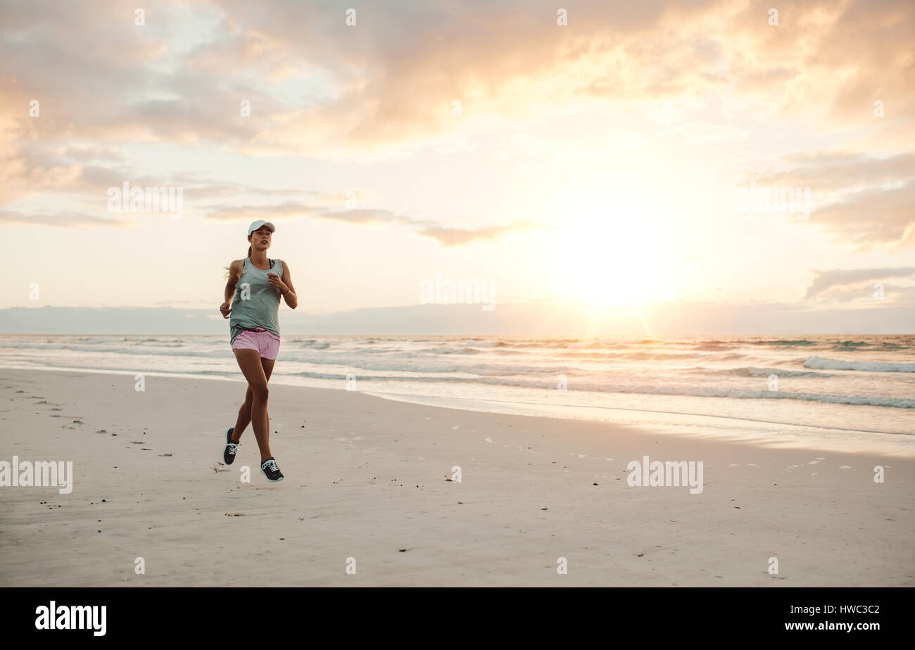 A piena lunghezza shot di montare la giovane donna in esecuzione sulla spiaggia di mattina. Femmina sano jogging sulla riva del mare. Foto Stock