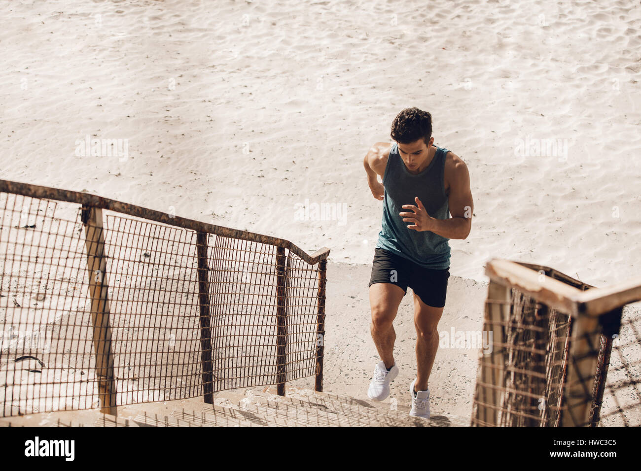 Montare il giovane uomo che corre in alto la scala sulla spiaggia. Giovane maschio runner lavoro su passi sulla riva del mare. Foto Stock