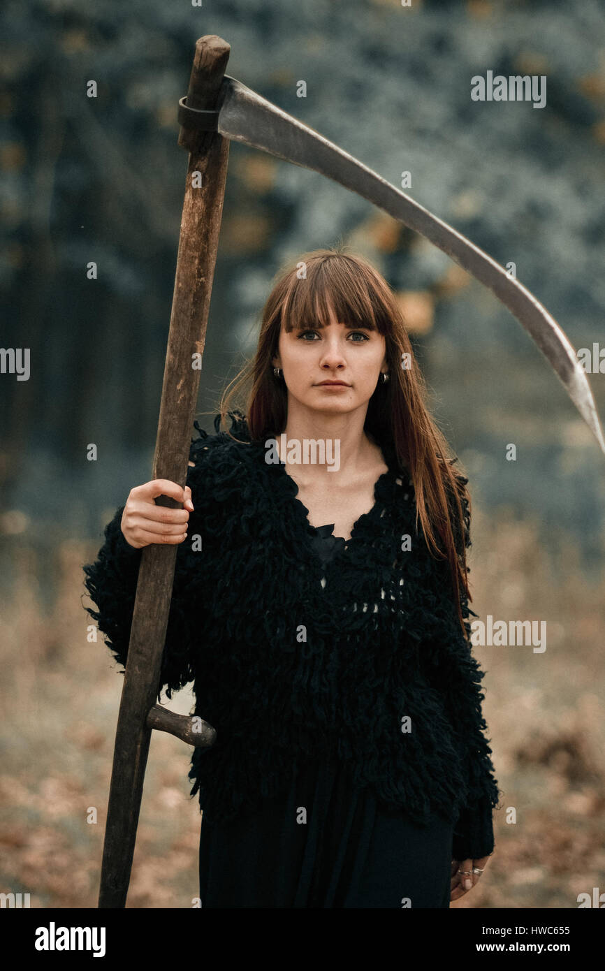 Primo piano immagine di abbastanza grave bellissima ragazza con i capelli lunghi vestiti di nero con intreccio sul bosco scuro dello sfondo. Grave ragazza mistico con seri Foto Stock