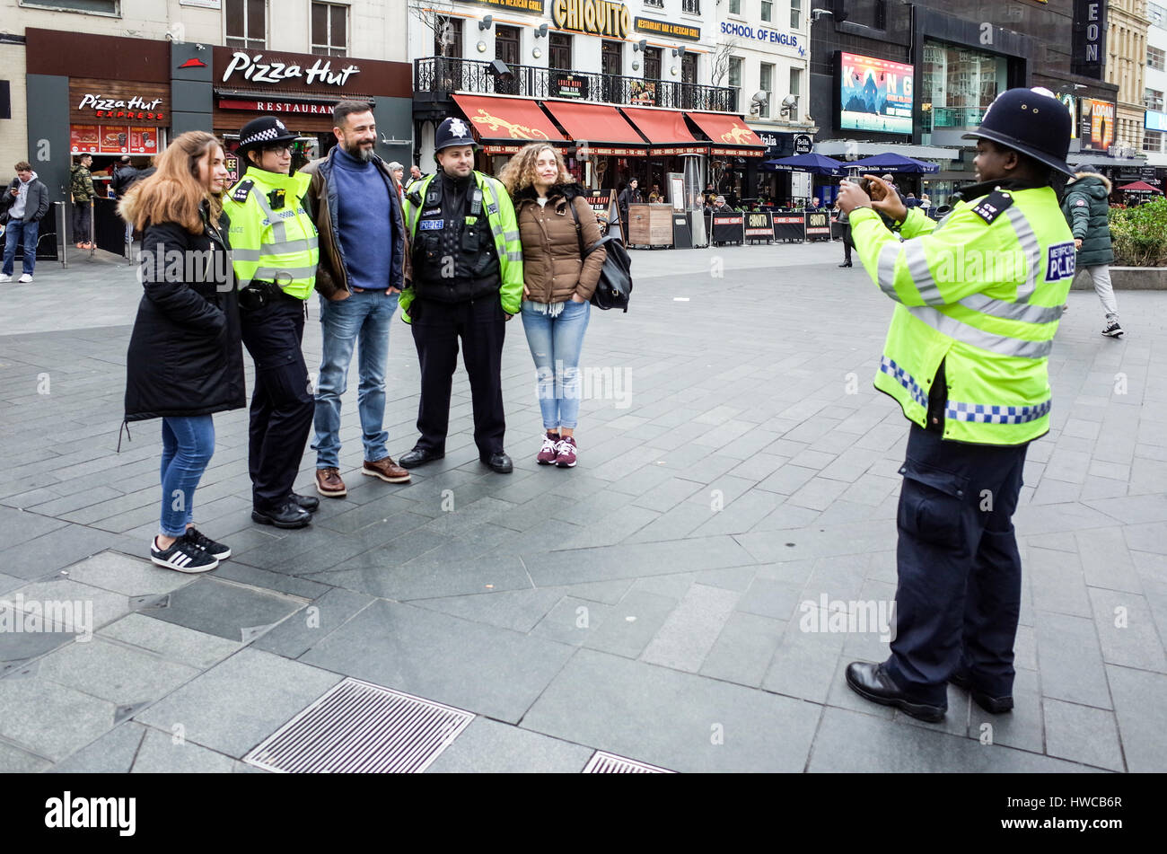 Friendly British Police - il poliziotto britannico scatta una foto per i turisti in piedi con i suoi colleghi a Leicester Square Londra. Amichevole Bobby britannico. Foto Stock