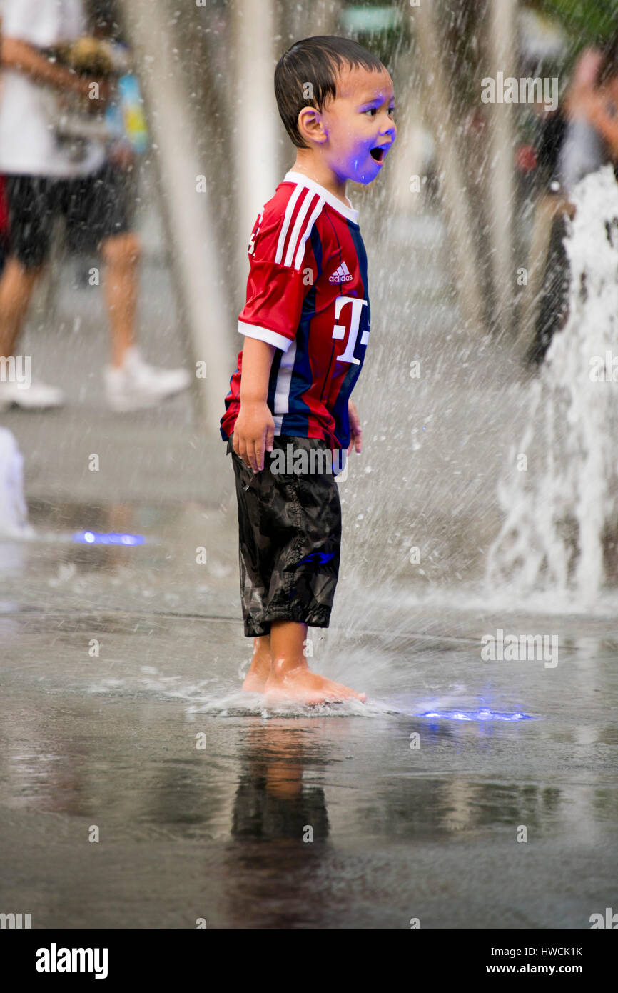 Ritratto verticale di un ragazzino giocando in Piazza Fontana in Singapore. Foto Stock