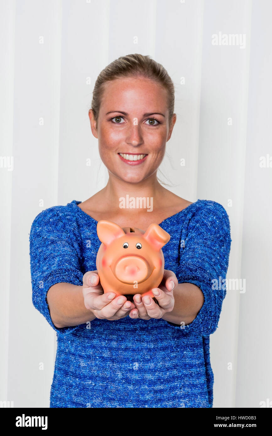 Una giovane donna detiene un modo divertente di maiale nella sua mano. Foto simbolico messo su per scherzi, il denaro e la vecchiaia disposizioni., Eine junge Frau h‰lt ein Sparschwein in ih Foto Stock