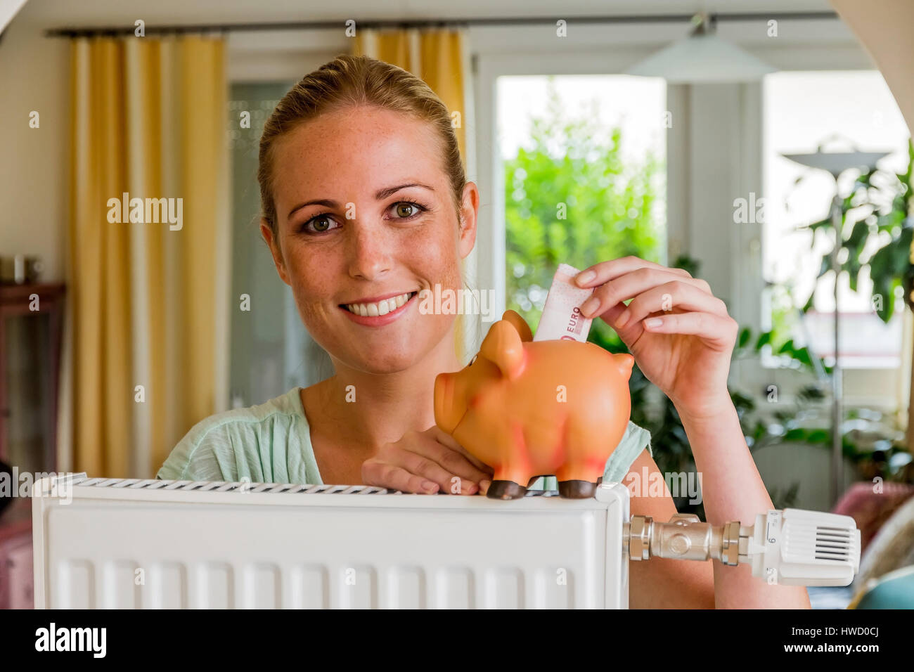 Una giovane donna con un riscaldatore e un maiale di divertimento. Foto simbolico per scherzare con energia e riscaldamento, Eine junge Frau Mit einem Heizkˆrper und einem Sparschwe Foto Stock