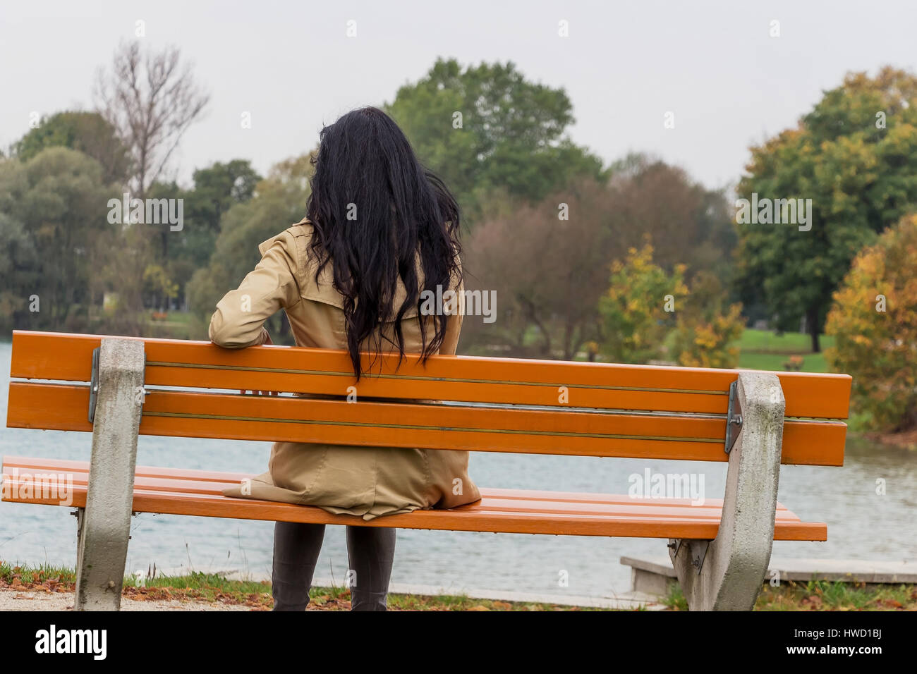 Una giovane donna siede pensieroso su un parco-banco, Eine junge Frau sitzt nachdenklich auf einer Parkbank Foto Stock