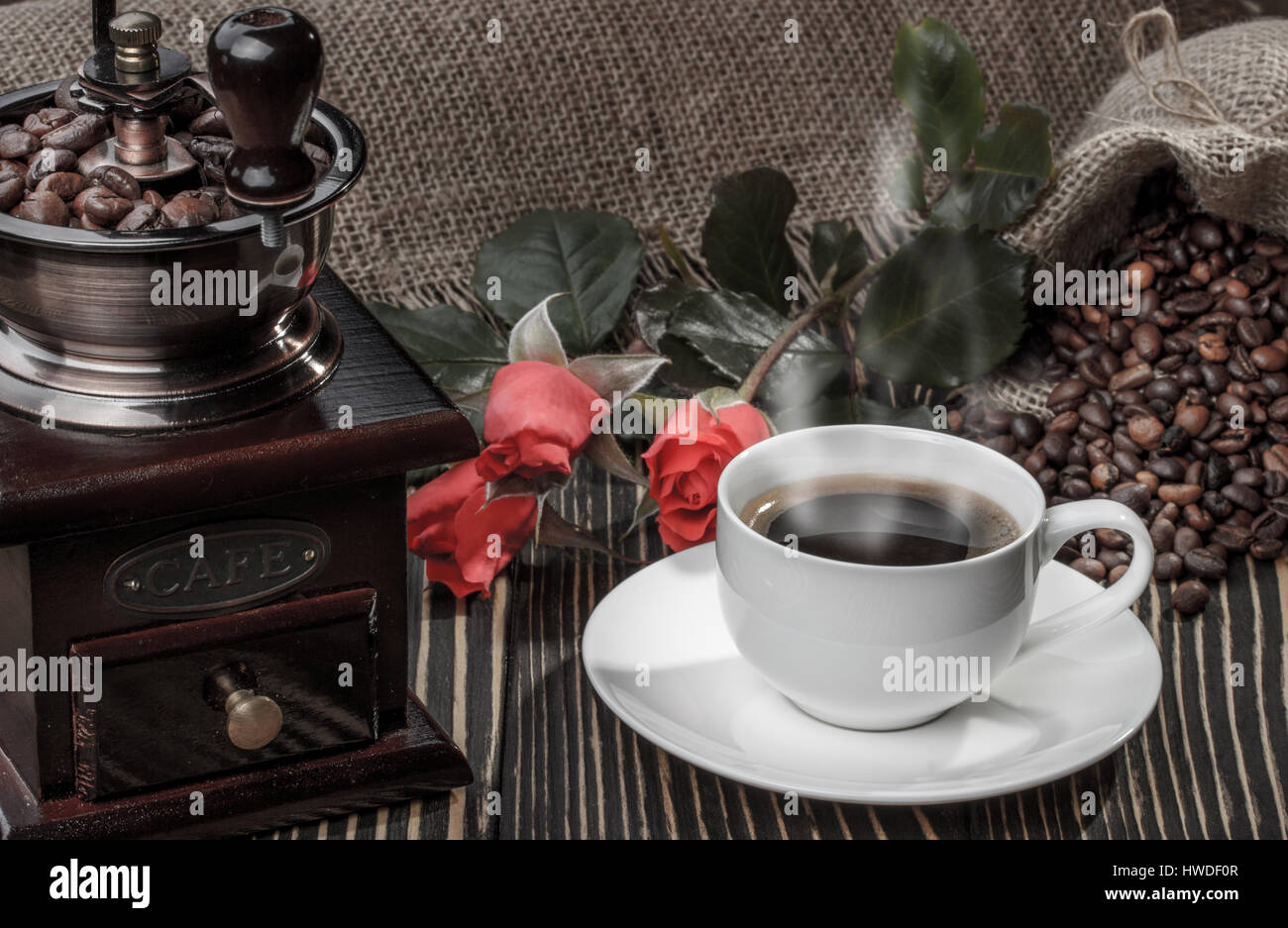 Macinino da caffè,rosa rossa e la tazza di caffè sulla vecchia scrivania in legno Foto Stock