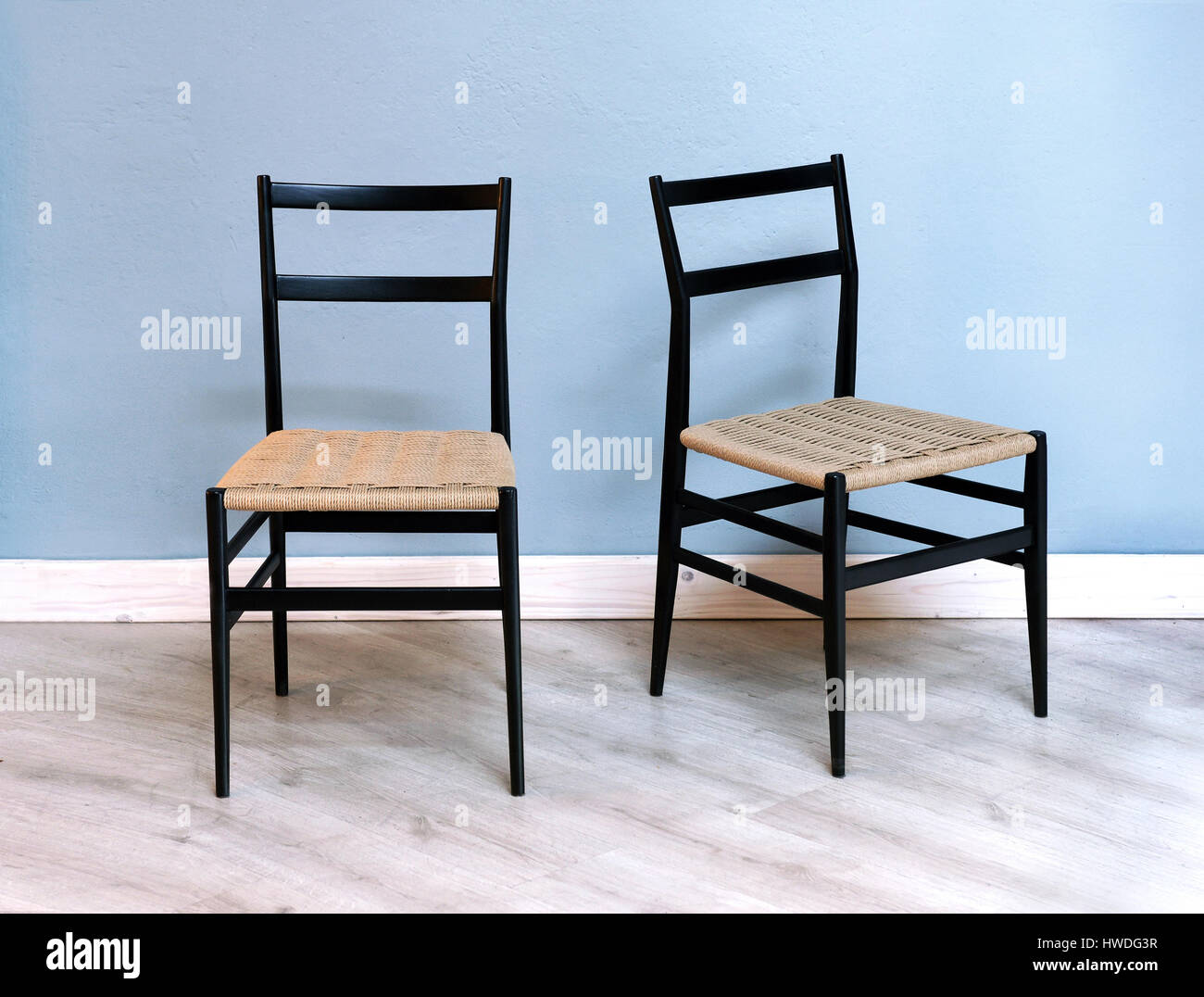 Due semplici cucina nera o sedie da pranzo con tessuto sedili in vimini contro una parete blu su bianco verniciato parquet Foto Stock