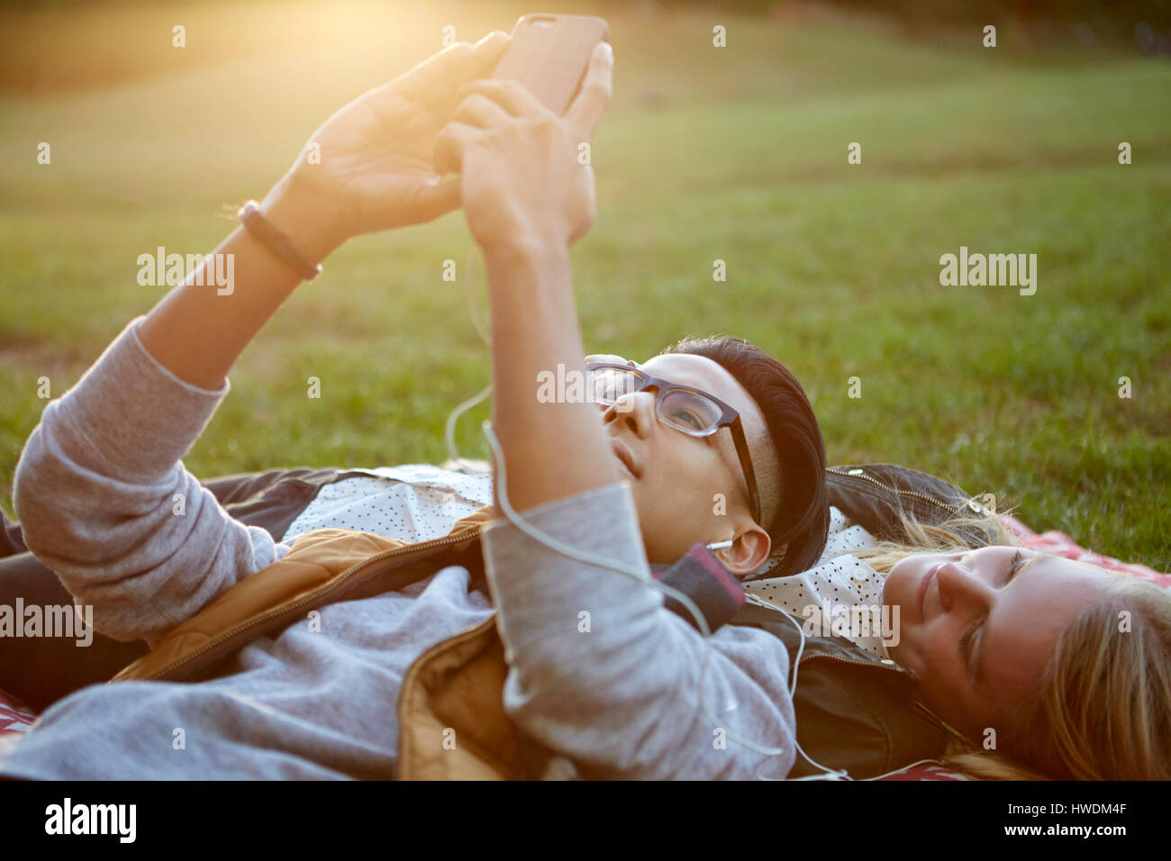 Giovane sulla coperta picnic nel parco di auricolari per la condivisione di musica Foto Stock