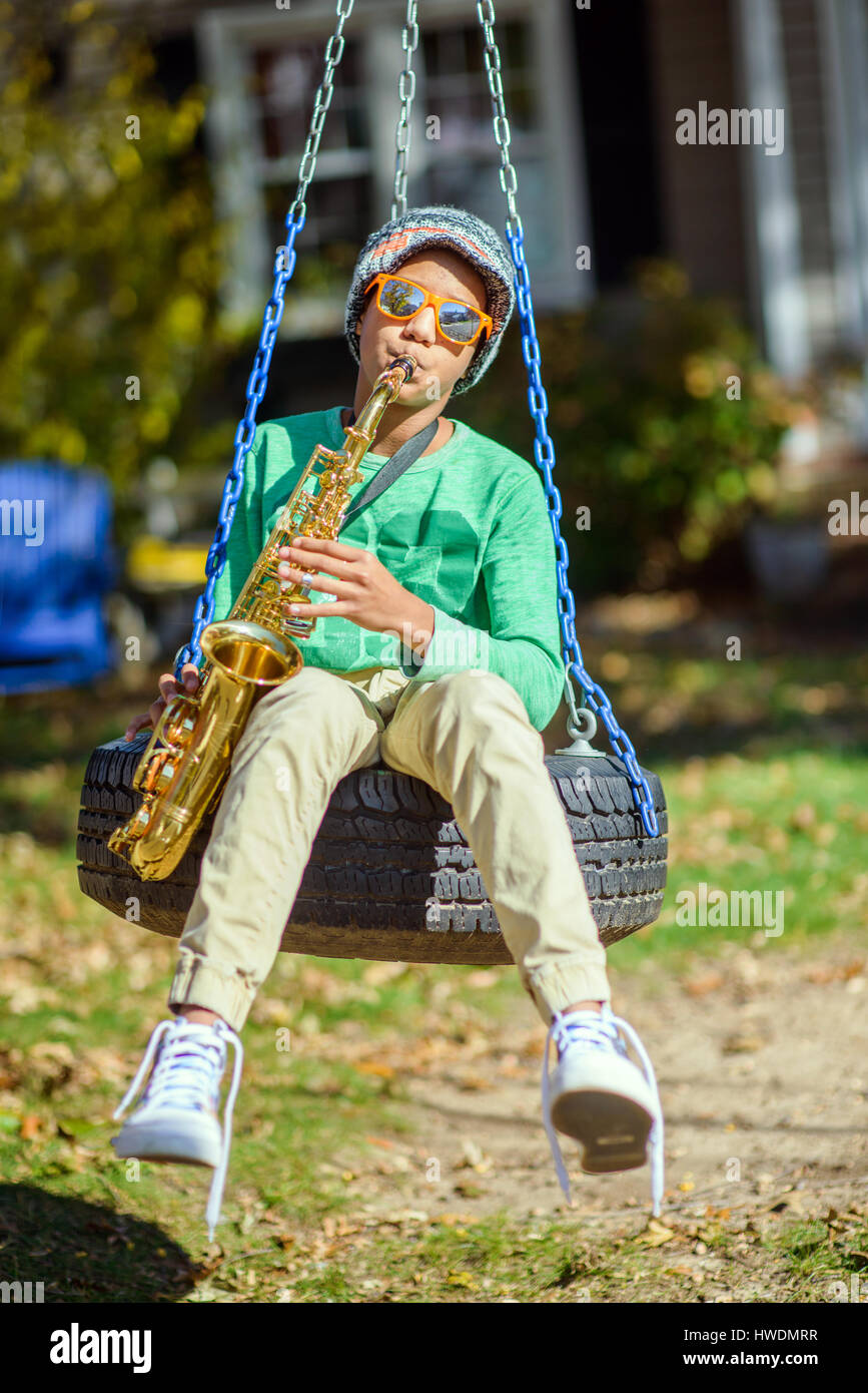 Ragazzo adolescente, seduti su tire swing, suonare il sassofono Foto Stock