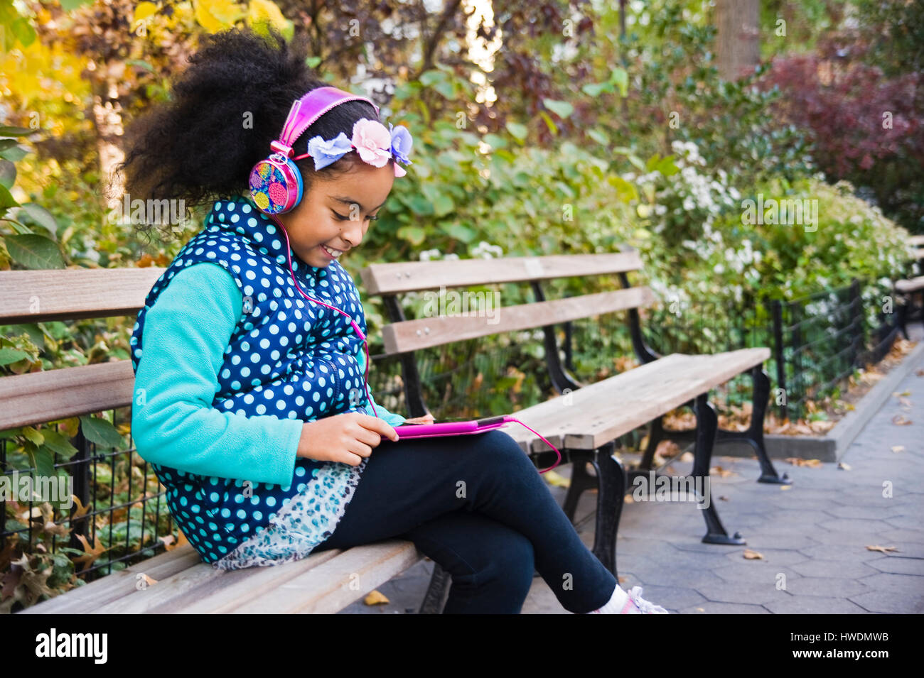 Ragazza seduta su una panchina nel parco che indossano le cuffie utilizzando tavoletta digitale Foto Stock