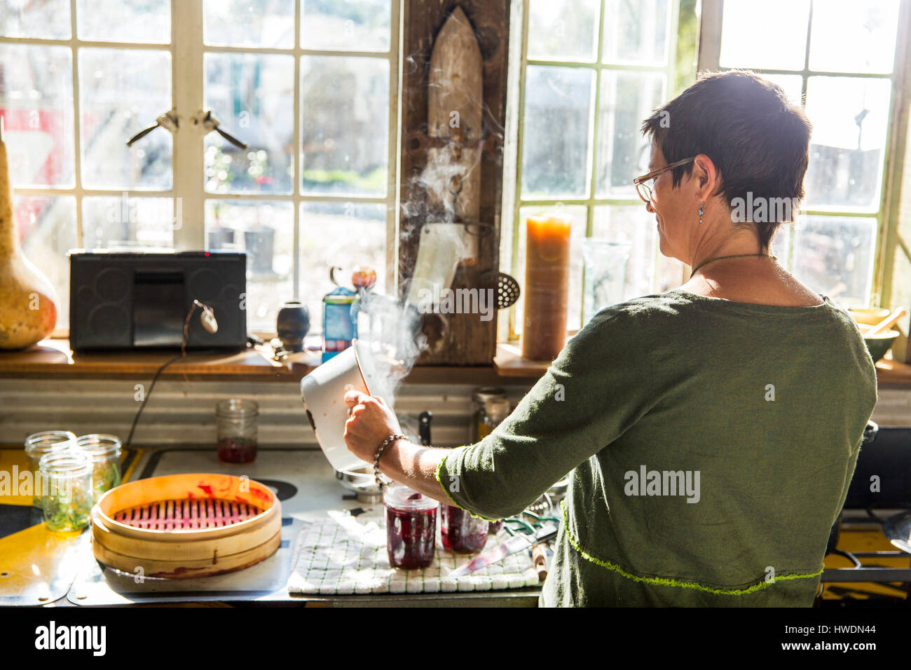 Vista posteriore della donna versando la barbabietola in conserva vasi in cucina Foto Stock