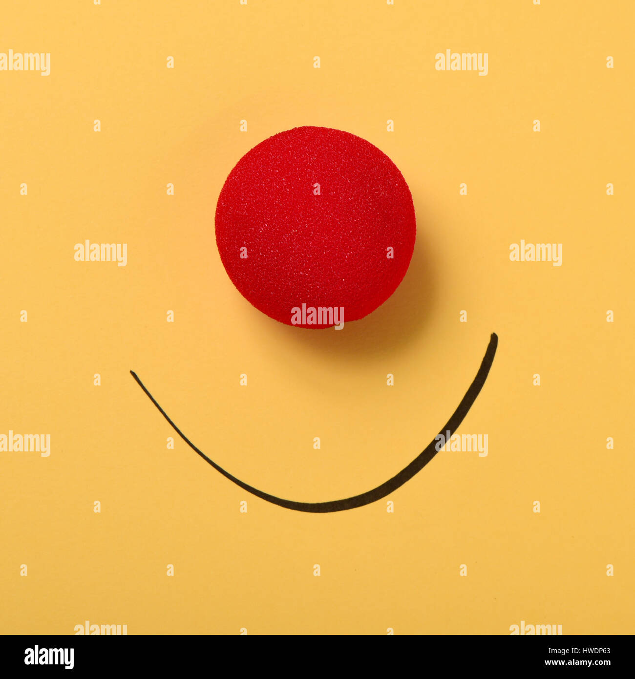 Un rosso clown naso e un sorriso disegnato su uno sfondo giallo Foto Stock
