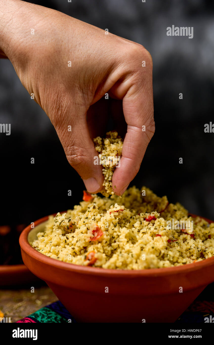 Primo piano di un giovane uomo di ottenere alcuni tabulé, un tipico levantine insalata araba, con la sua mano da un recipiente di terracotta collocato su un tavolo per il pranzo Foto Stock