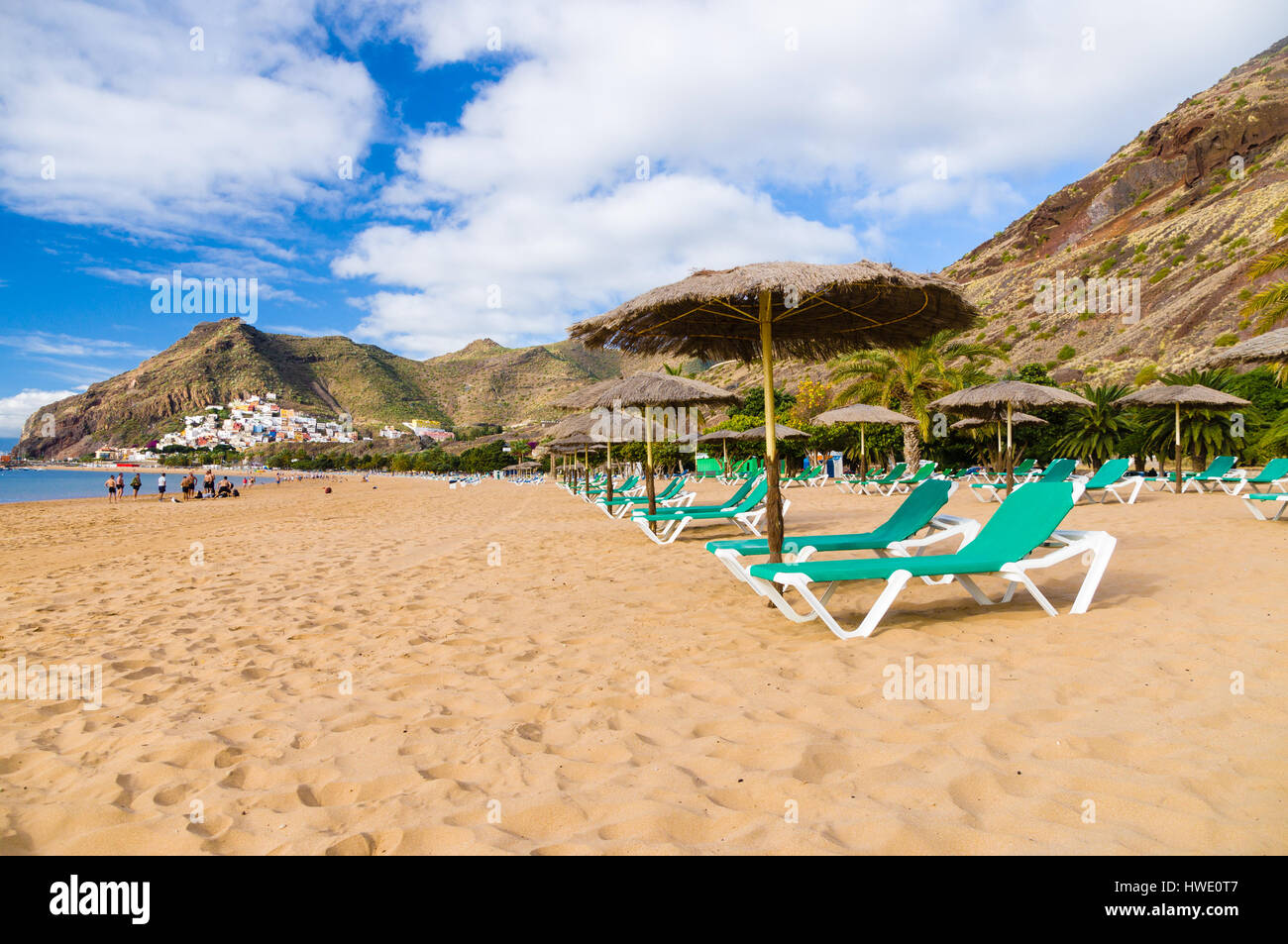 Palapa e chaise-longue sulla sabbia dorata di Playa de Las Teresitas. San Andres villaggio su sfondo, Tenerife, Spagna Foto Stock