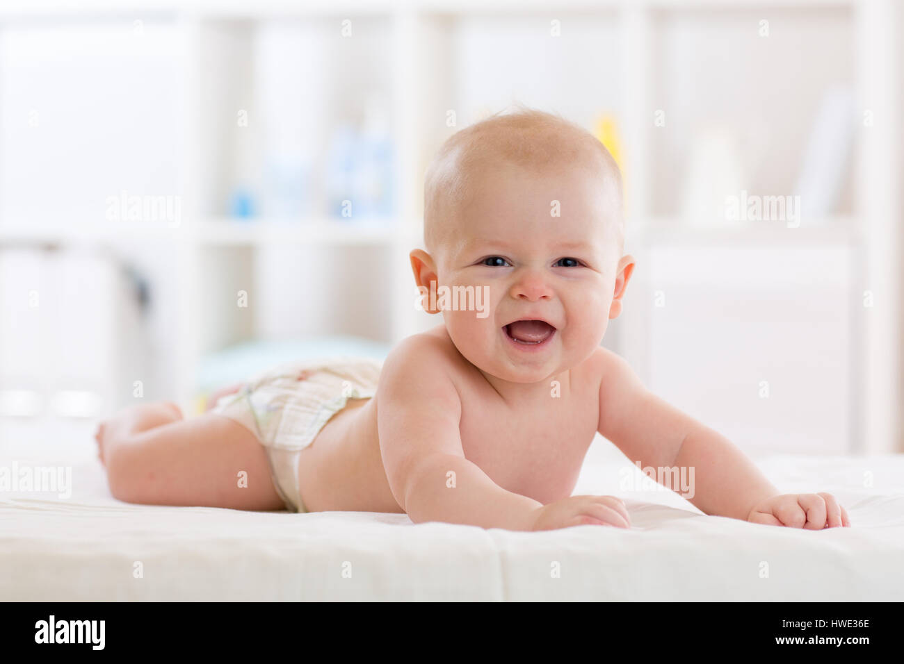 Baby boy indossa pannolino in bianco e luminosa camera da letto. Bambino neonato rilassante nel letto Foto Stock