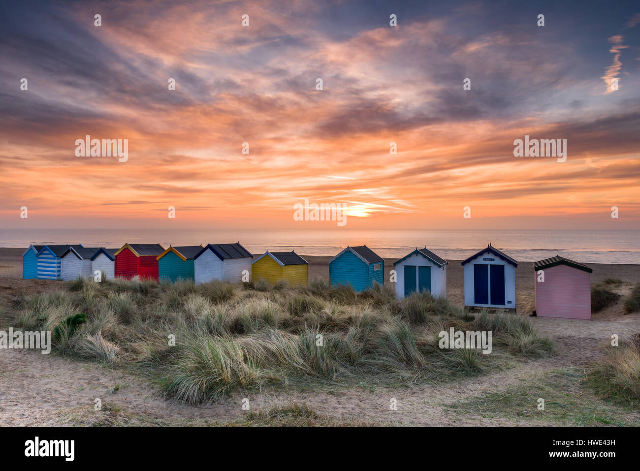 Su una calma alba a metà marzo, il sole sorge oltre la famosa linea di cabine sulla spiaggia, sulle dune a Suffolk cittadina balneare di Southwold. Foto Stock