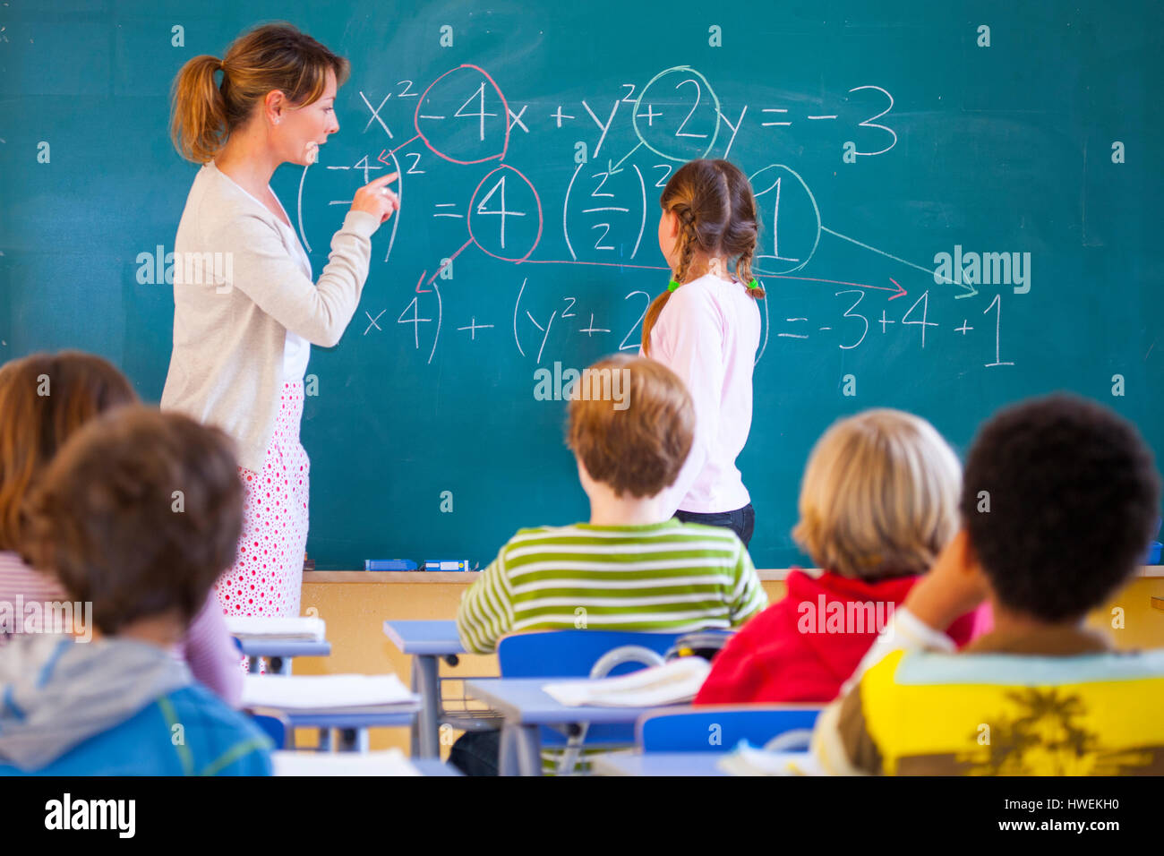 L'insegnante di scuola primaria che spiega l'equazione sulla lavagna in aula Foto Stock