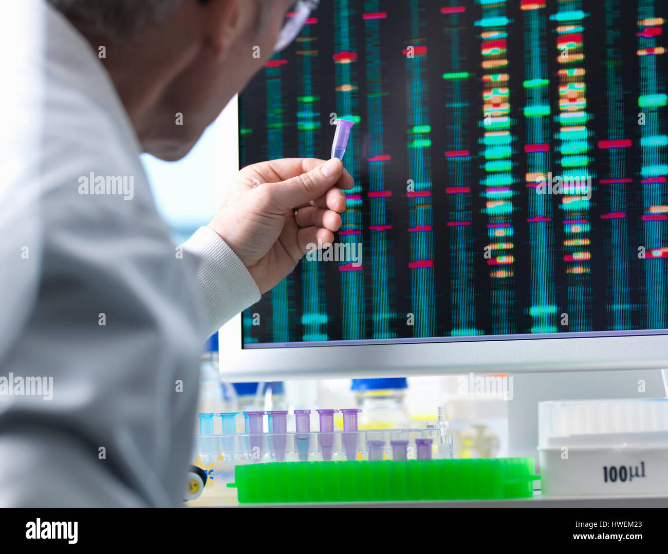 Ricerca di DNA, scienziato tenendo su un campione di DNA con i risultati sullo schermo del computer Foto Stock