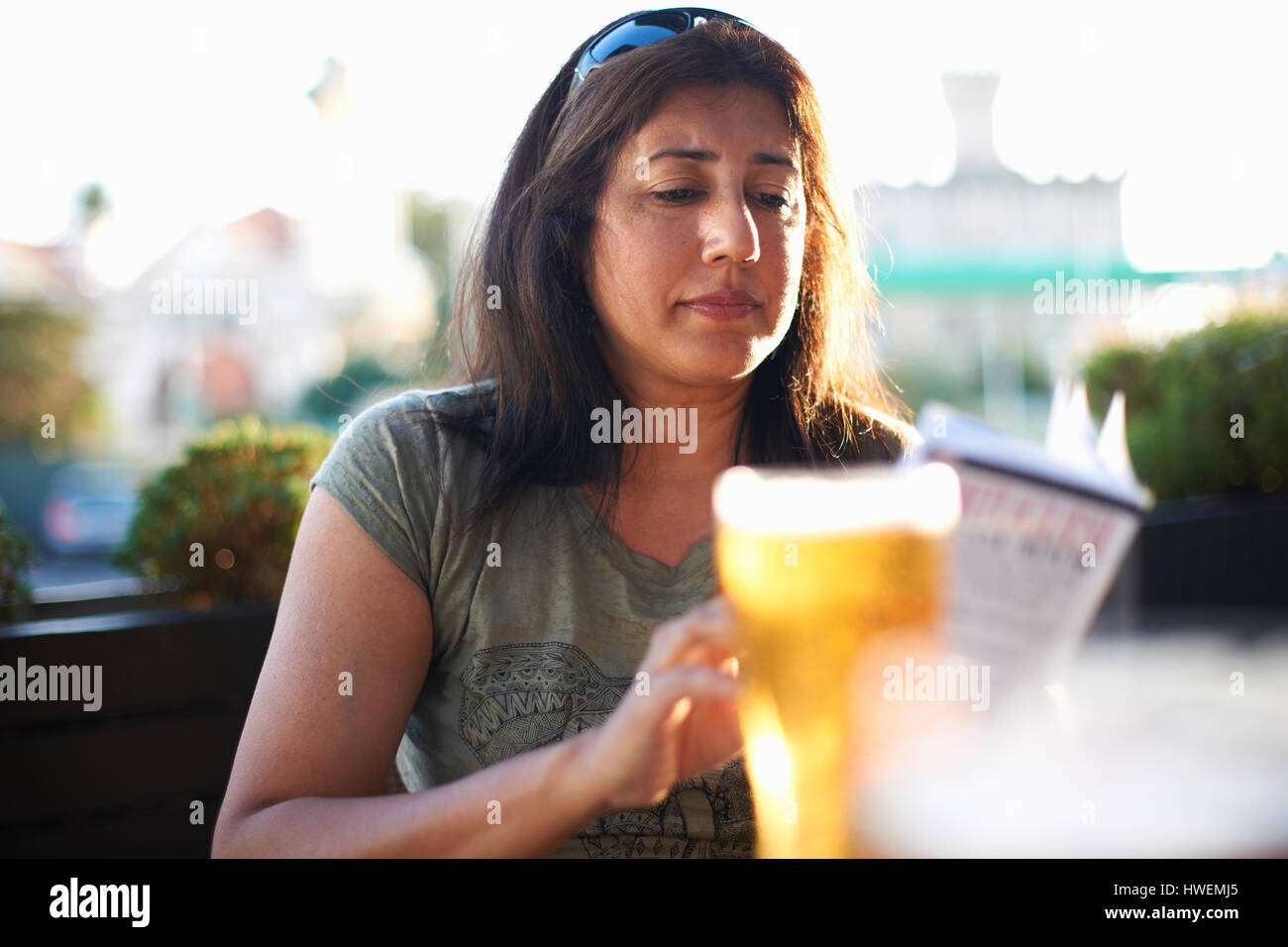 Donna matura leggendo la guida al cafè sul marciapiede, Cascais, Portogallo Foto Stock
