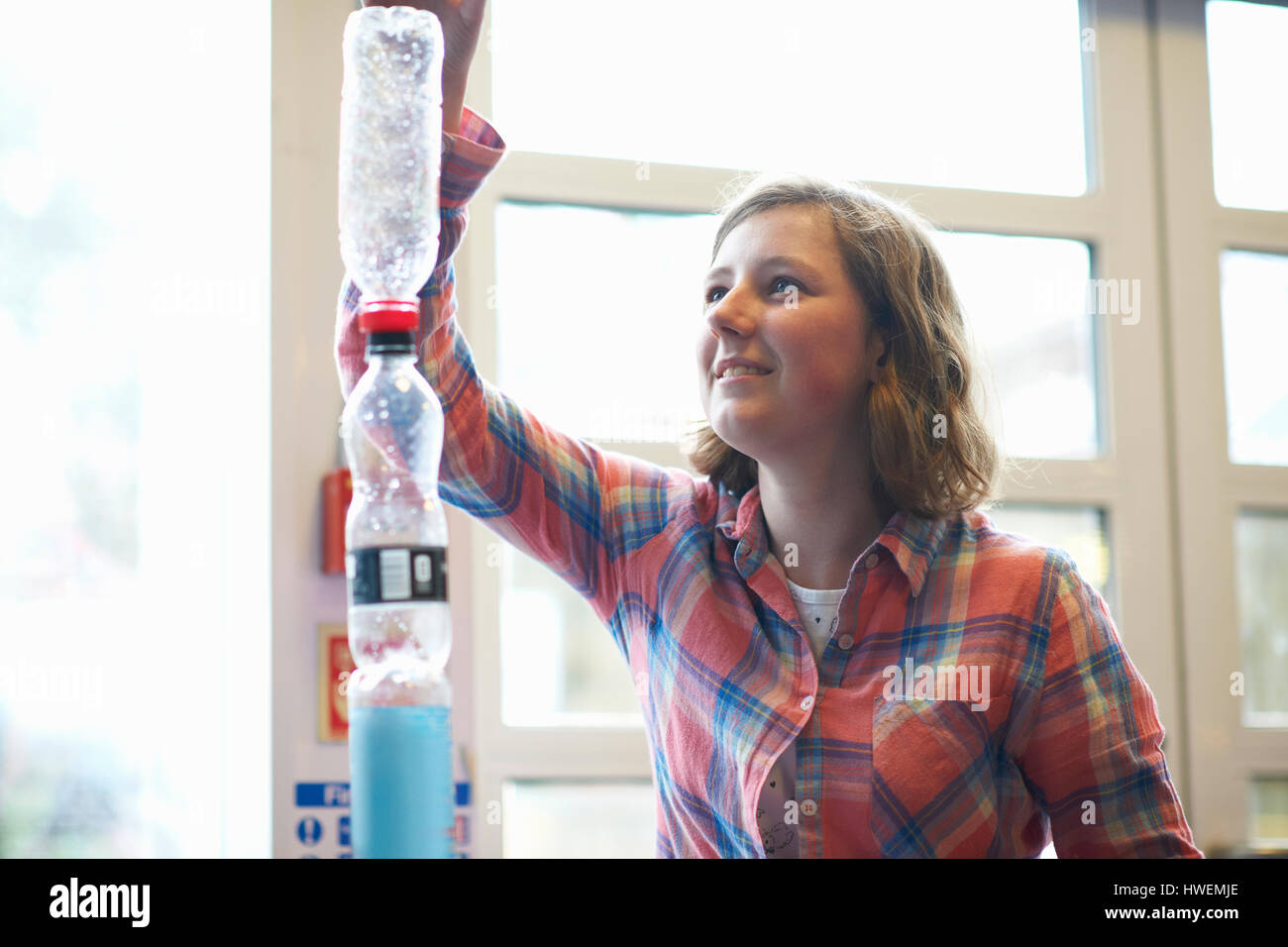 Teenage studentessa di impilamento di bottiglie di plastica per l'esperimento in college classroom Foto Stock