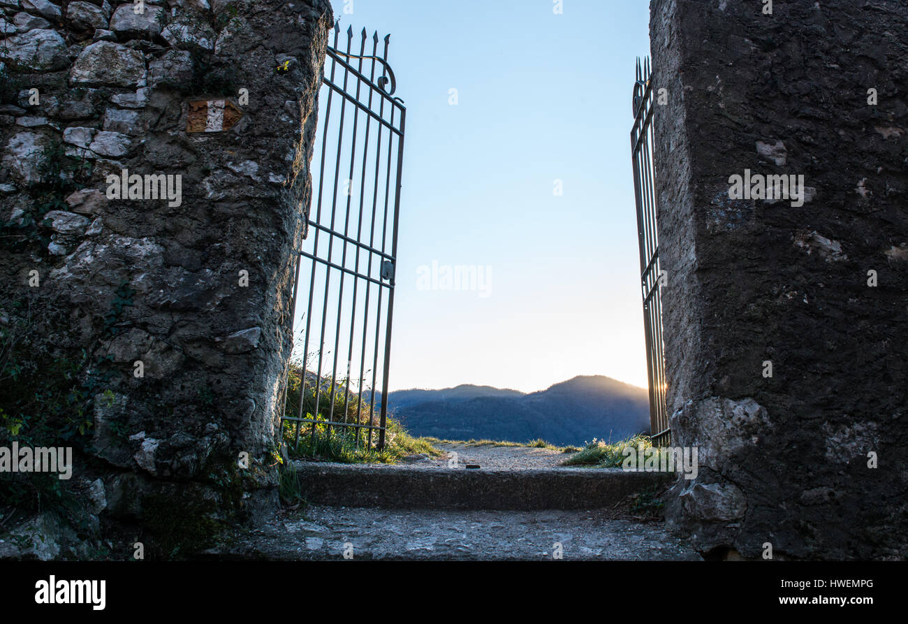 I muri di pietra e vecchi cancelli aperti con vista in lontananza le montagne al tramonto Foto Stock