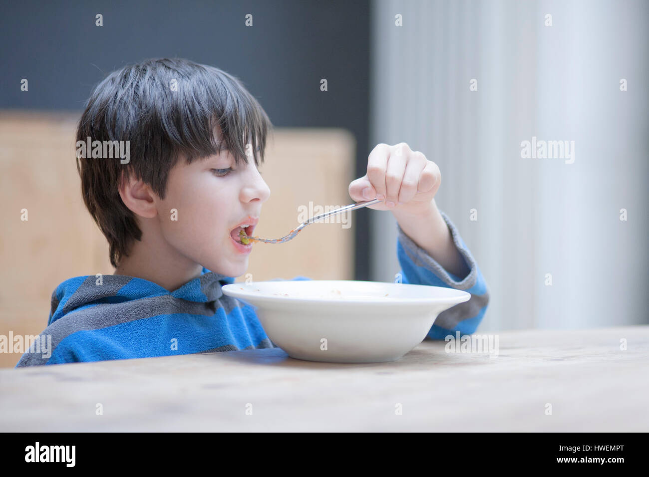 Ragazzo di mangiare il pranzo da coppa al tavolo della cucina Foto Stock