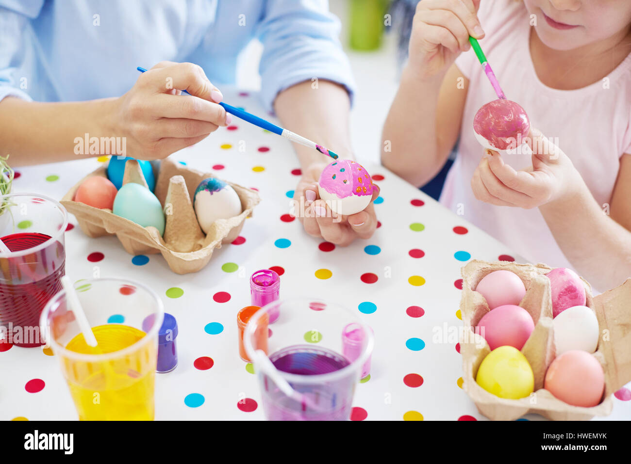 Ritagliato colpo di donna e di mia figlia mani di pittura delle uova di pasqua a tavola Foto Stock